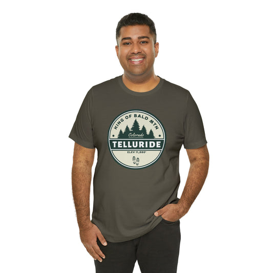 Green t-shirt with a circle design featuring black lettering saying "King of Bald Mtn.", Telluride, CO. and Elevation 11,880'. The t-shirt is made of 100% cotton and is perfect for a day of skiing or snowboarding at Telluride Ski Resort. The phrase "King of Bald Mtn." is a popular saying among skiers and snowboarders who have summited Bald Mountain, a mountain in Telluride, Colorado. This t-shirt a great way to show your support for the resort and the apres ski lifestyle.