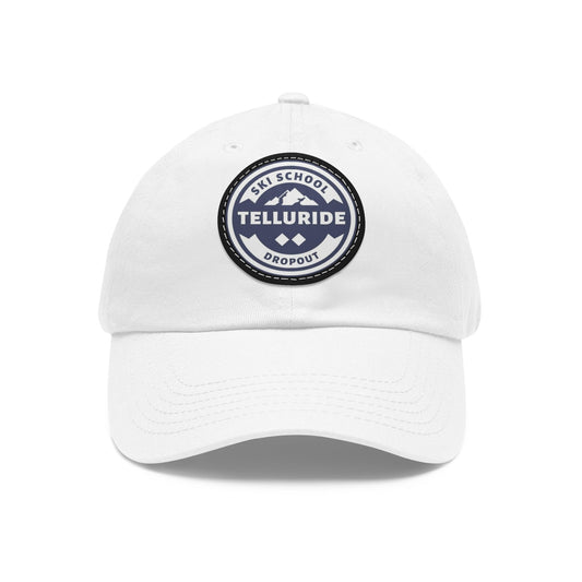 White dad hat with a blue leather patch circle featuring black lettering saying "Ski School Dropout" and Telluride, and two ski sign diamonds. The hat is made of 100% cotton and is perfect for keeping the sun out of your face while you're skiing or snowboarding at the Telluride Ski Resort. This hat is a great way to show your love of skiing and snowboarding, and your love of Telluride.