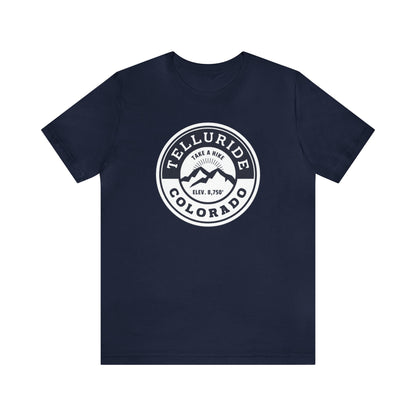 Unisex short sleeve t-shirt with a circle navy and white logo featuring white lettering saying "Telluride, Colorado", "Take A Hike", and "Elev. 8,750". The t-shirt is made of 100% cotton and is perfect for a day of hiking or skiing. The phrase "Take A Hike" is a popular saying among hikers and skiers, and the words "Telluride, Colorado" represent the beauty of the Telluride Ski Resort. This t-shirt is a great way to show your love of the outdoors and your love of Telluride.