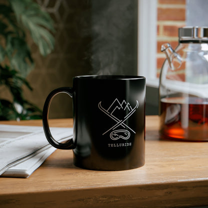 Black coffee mug with crossed skis, mountains, and ski or snowboard goggles, with the word "Telluride" printed on the mug. The mug is a stylish and fun way to show your love of skiing and the Telluride Ski Resort. The crossed skis represent the sport of skiing, the mountains represent the beauty of Telluride, and the ski or snowboard goggles represent the fun of being outdoors. The mug is a great way to enjoy a hot beverage while relaxing and dreaming of your next ski trip.