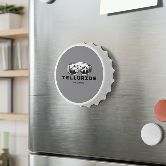 White magnetic bottle opener with a grey circle printed on it and the words "Telluride" and "Colorado" printed in black. The circle contains an image of mountains inside of ski or snowboard goggles. The bottle opener is a stylish and functional way to show your love of skiing, snowboarding and Telluride.  The bottle opener is a great way to open a cold drink after a day on the slopes at the Telluride Ski Resort.