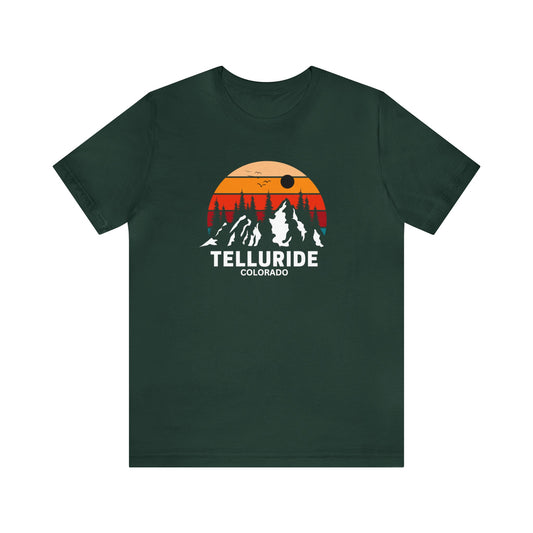 Green short sleeve unisex t-shirt with white lettering saying "Telluride Colorado". The t-shirt also has a colorful image of the mountains and a sunset in the background. The t-shirt is a stylish and comfortable way to show your love of skiing, snowboarding, hiking or shopping at the Telluride Ski Resort. 