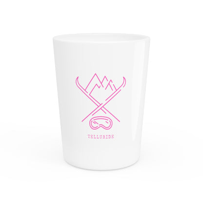 White ceramic shot glass with pink lettering saying "Telluride" and a mountain range in the background. The glass has a image of crossed skis and ski goggles. The glass is a stylish and practical way to enjoy a shot of your favorite spirit while celebrating your love of the Telluride Ski Resort and Colorado.