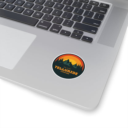 Green circle sticker with orange lettering saying "Telluride Colorado" and a colorful image of the mountains and a sunset in the background. The sticker is a stylish and unique way to show your love of skiing, snowboarding, hiking or shopping at the Telluride Ski Resort whether you're sticking it on your laptop, or water bottle.